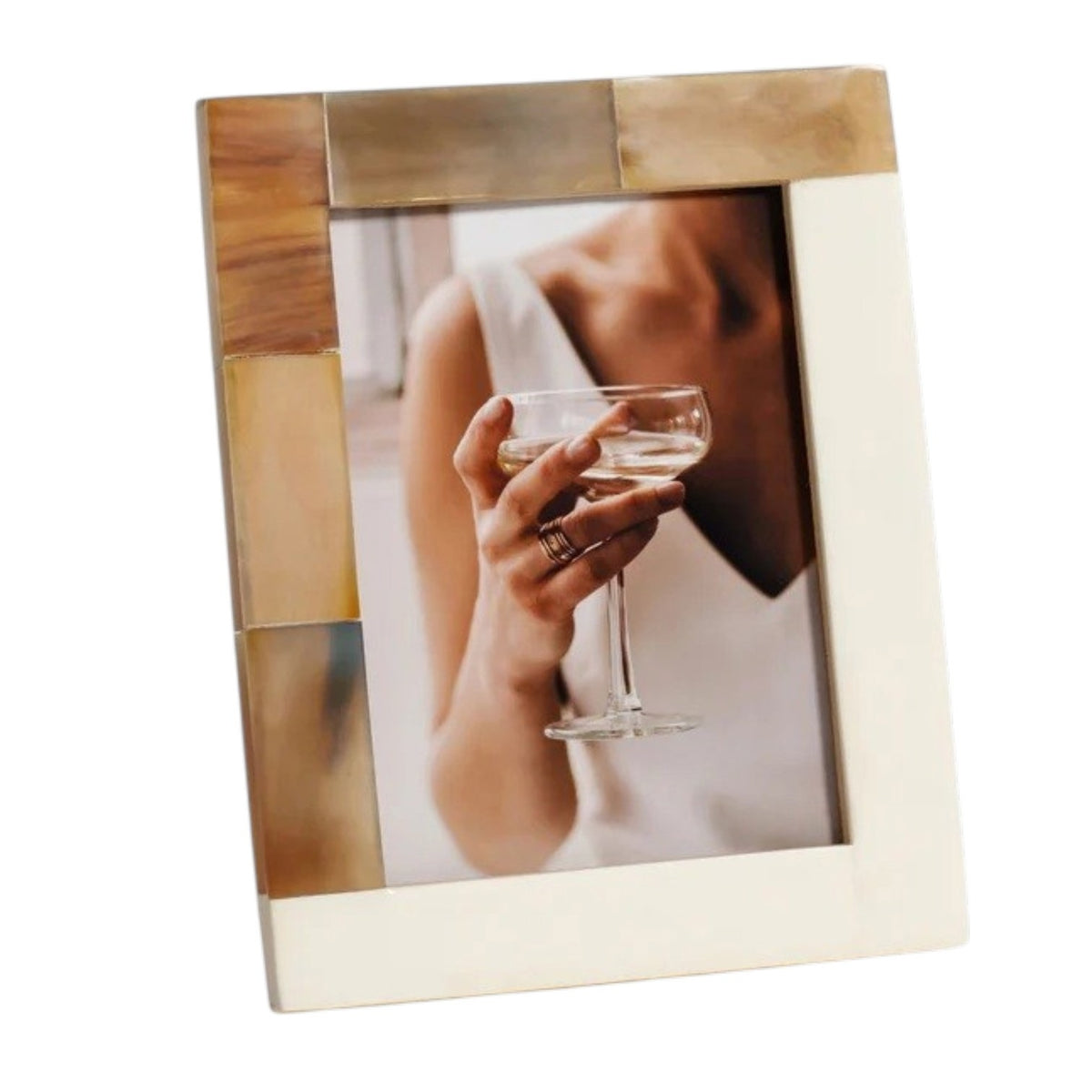 Two luxury ZODAX photo frames—one crafted from natural white horn inlay and the other an elegant ivory resin—display portraits: one shows a person holding a glass, while the other features a close-up of a face with a finger touching the lips. Both WHITE HORN AND IVORY RESIN FRAME - 5X7 rest on a patterned surface.