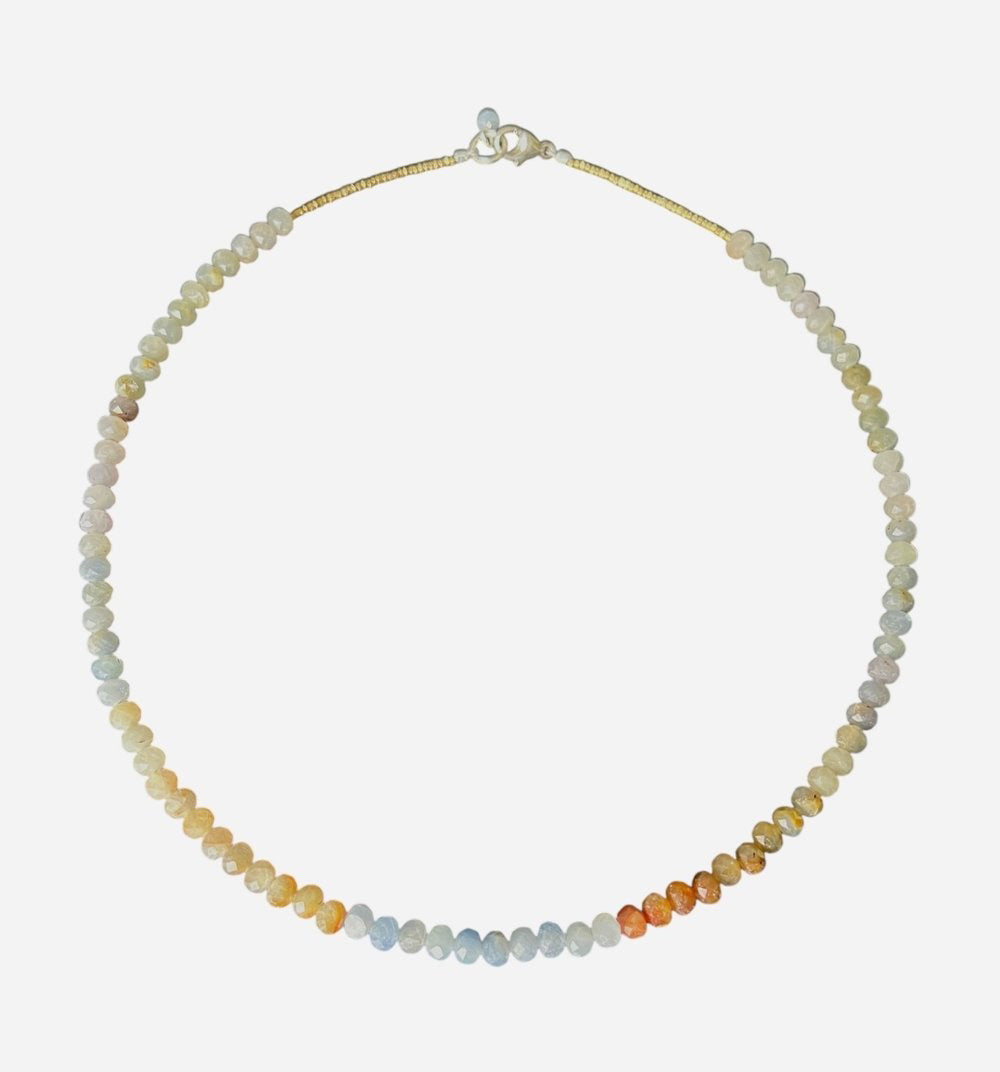 A woman wears the ANN LIGHTFOOT Multi Color Sapphire Ras Du Cou Necklace—a beaded choker by ANN LIGHTFOOT—paired with a textured beige sweater; the image highlights her neck and lower face.