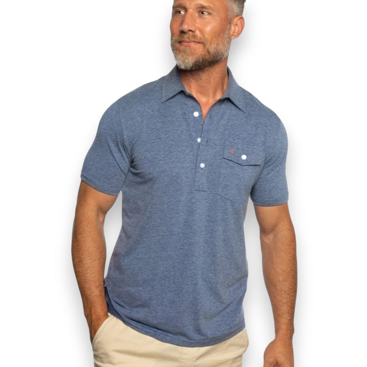 A man with short gray hair and a beard wears the CRIQUET Performance Players Shirt in Midnight, a moisture-wicking classic fit polo with a chest pocket, paired with light pants. He stands with one hand in his pocket against a white background.