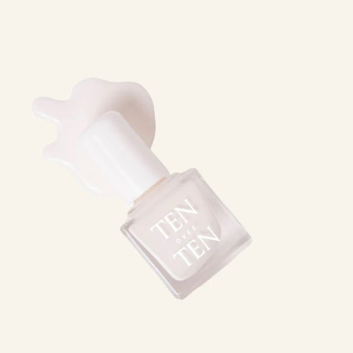 A glass bottle of TENOVERTEN - NAIL POLISH from the brand TEN OVER TEN, featuring a white cap and a dusty pink nail color. The front label displays "TEN OVER TEN" in white uppercase letters. This vegan, eight-free formula ensures both beauty and peace of mind. The background is plain and light-colored.
