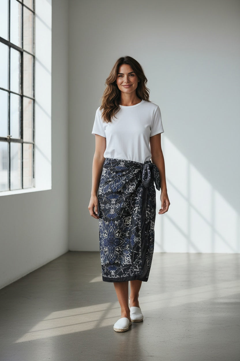 The MAISON LECOMTE - COSTA BRAVA BLACK SARONG by MAISON LECOMTE FLAMENT, featuring a white and blue paisley pattern, is tied in a loose knot against a plain white background.