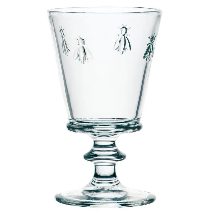 The LA ROCHERE BEE WATER GLASS, with its embossed Napoleonic bee, rests on a sunlit table beside a green lime drink, fresh cantaloupe slices, and white flowers for an effortlessly elegant display.