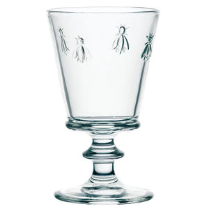 The LA ROCHERE BEE WATER GLASS, with its embossed Napoleonic bee, rests on a sunlit table beside a green lime drink, fresh cantaloupe slices, and white flowers for an effortlessly elegant display.