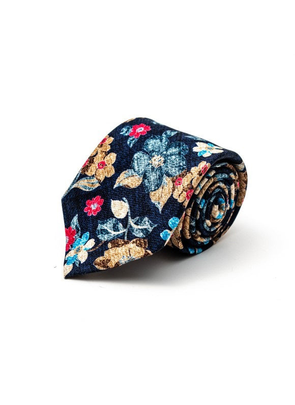 The EDWARD ARMAH - NAVY FLORAL SILK TIE features a navy blue background with a vibrant red, yellow, blue, and white floral pattern. Displayed rolled up on a white surface, this stylish tie is crafted by EDWARD ARMAH.