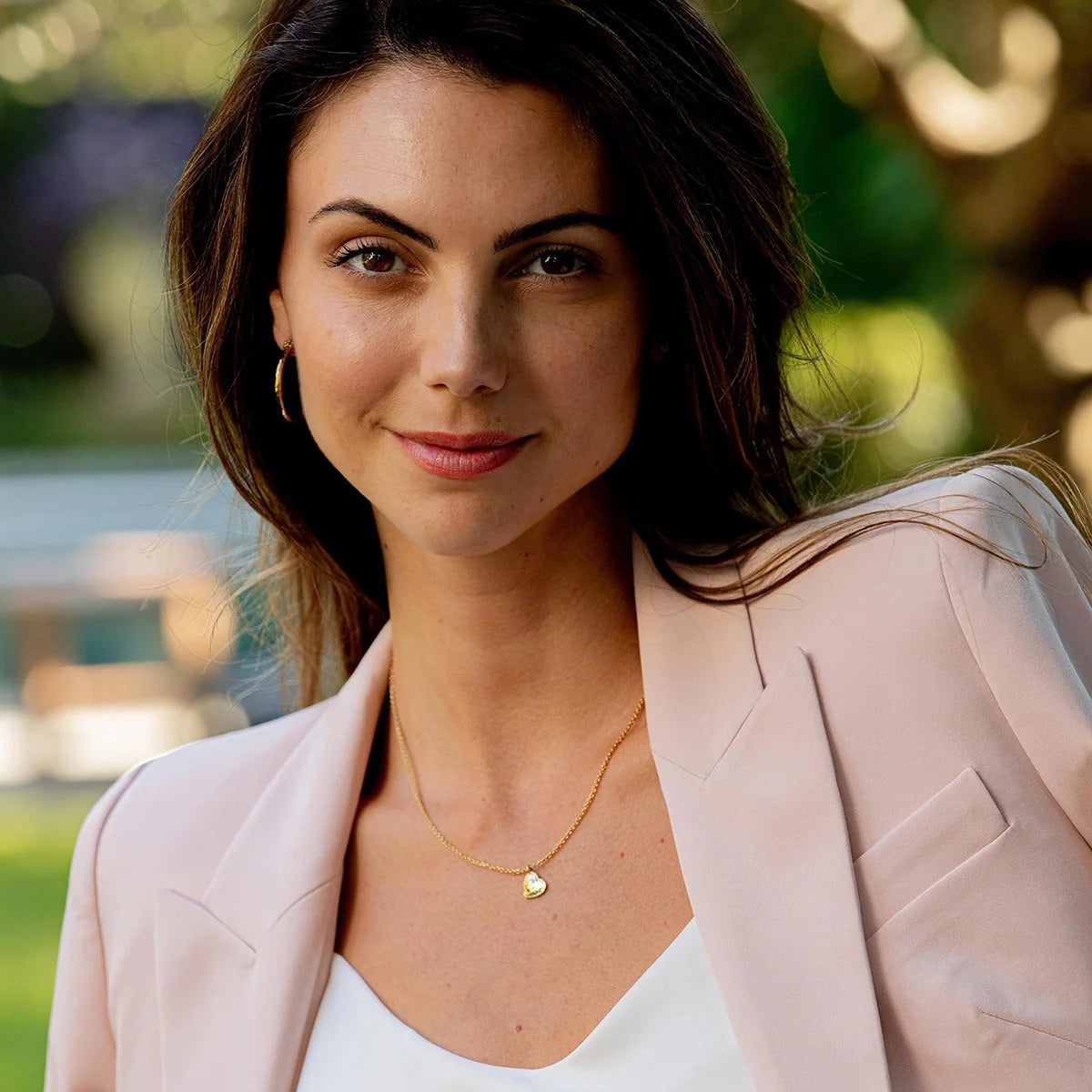 The CAPUCINE DE WULF - LOVE HEART CHARM NECKLACE by CAPUCINE DE WULF features a delicate gold chain with a small, heart-shaped pendant engraved with an intricate design, displayed against a plain white background. This elegant handcrafted piece is perfect for adding everyday sophistication to your jewelry collection.