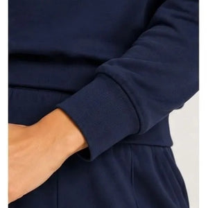 A woman wears a SOFTIES - DREAMTECH BOAT NECK WITH PINTUCK PANT SET in olive green, featuring a long-sleeve boat neck top and matching wide-leg pintuck pants.