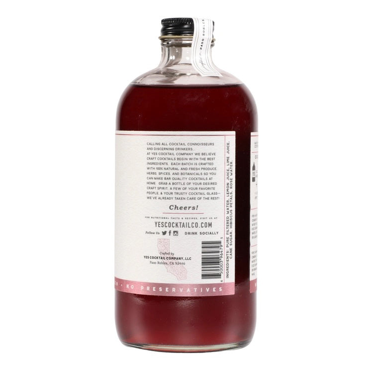 A transparent glass bottle holds a rich, dark red liquid labeled "YES COCKTAIL CO - Hibiscus Rose Cocktail Mixer." Handcrafted in California and available in a 16 fl oz (473ml) size, the white-and-red-toned label indicates its perfect suitability for creating cocktails or an exotic floral spritzer.