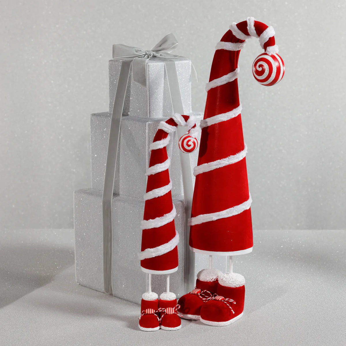 The ZODAX WHIMSICAL CANDY CANE HAT FIGURE is a tall red hat with white trim and spiral stripes, standing on two legs in red shoes. Measuring 10.16 x 48.26 cm, it features a curled tip with a peppermint ornament.