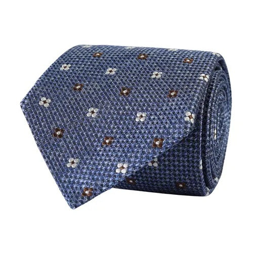 The AMANDA CHRISTENSEN - FLORAL JACQUARD WOVEN SILK TIE IN BLUE MELANGE features a refined blue hue with a subtle checkered pattern and scattered white and brown floral motifs. Rolled up on a white background, this sophisticated tie from AMANDA CHRISTENSEN is perfect for elevating your collection of men’s accessories.
