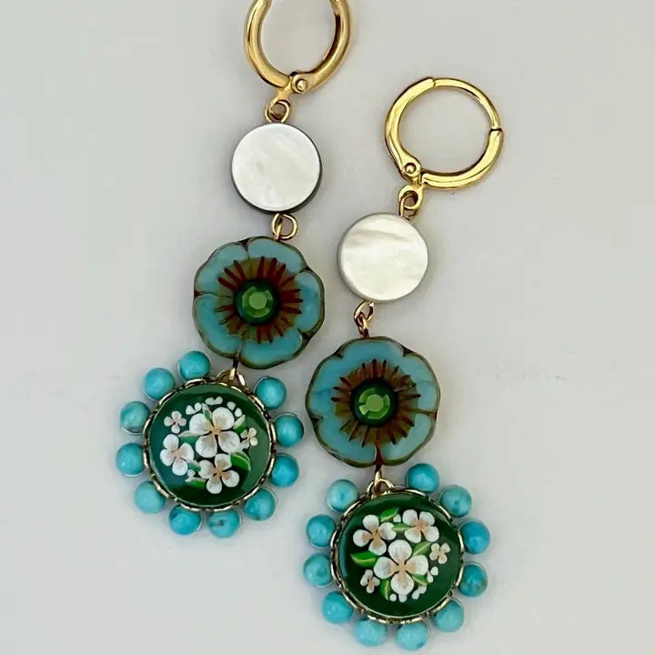 The SANDRINE FRANCE STUDIO - MOLLY EARRINGS by SANDRINE FRANCE STUDIO are handmade in NYC, featuring gold hoops with white discs, blue-green floral beads, brown centers, green pendants, vintage Japanese glass, and turquoise accents.