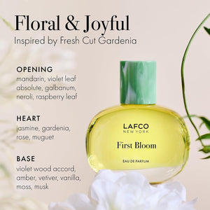 A box of LAFCO - FINE FRAGRANCE, FIRST BLOOM 50ML stands among white flowers and green vines against a pale beige background.
