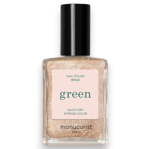A hand with medium-brown skin displays short, neatly manicured nails painted with MANUCURIST - GREEN™ NAIL POLISH IN GOLD by MANUCURIST INC, featuring a shimmery pale gold glitter finish against a neutral beige background.
