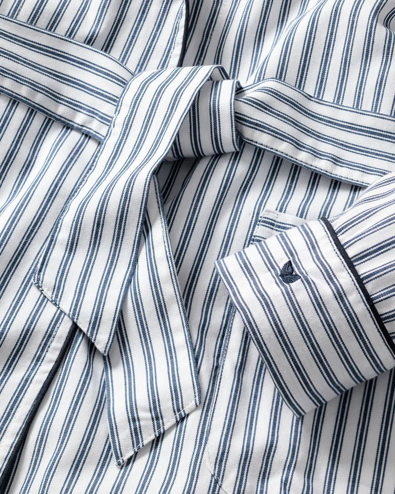 The FEARRINGTON LIFESTYLE COLLECTION - WOMEN&#39;S TWILL ROBE IN NAVY FRENCH TICKING by PETITE PLUME is a knee-length, long-sleeved robe with a tie belt at the waist. Crafted from the finest quality cotton, it features vertical navy and white stripes with matching striped cuffs on the sleeves. This piece of luxurious sleepwear boasts two front pockets and a shawl collar for added comfort.