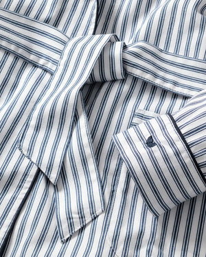 The FEARRINGTON LIFESTYLE COLLECTION - WOMEN'S TWILL ROBE IN NAVY FRENCH TICKING by PETITE PLUME is a knee-length, long-sleeved robe with a tie belt at the waist. Crafted from the finest quality cotton, it features vertical navy and white stripes with matching striped cuffs on the sleeves. This piece of luxurious sleepwear boasts two front pockets and a shawl collar for added comfort.