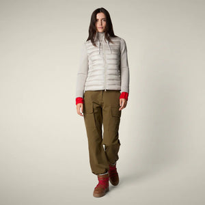 A woman with straight brown hair and a neutral expression models the SAVE THE DUCK - ZILIA JACKET in light gray, styled with olive cargo pants, red socks, and tan boots—showcasing effortless transitional layering.