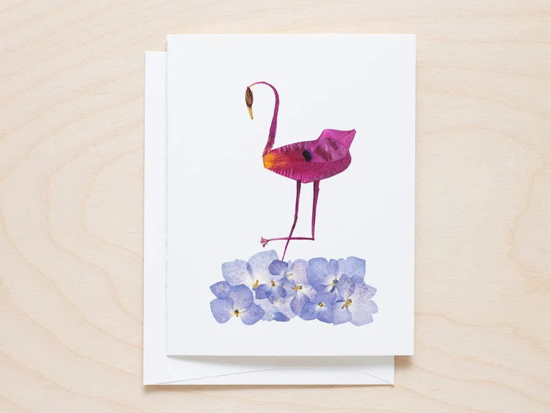 The PETAL PEOPLE PRESS - FLAMINGO CARD features a flamingo artfully made from vibrant purple petals, surrounded by whimsical light blue and pink flowers on a white background.