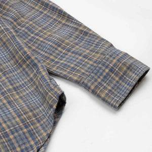A close-up of the HARTFORD - PAUL Checked Flannel Shirt in Grey highlights the blue, brown, and grey plaid cotton fabric, with a focus on the cuff and sleeve featuring visible white buttons.