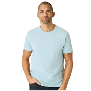 A man with short hair stands with his back to the camera, wearing the MACK WELDON Slub Cotton Crew Neck T-Shirt in Nile Blue Heather and dark pants. His hands are in his pockets as he glances over his left shoulder.