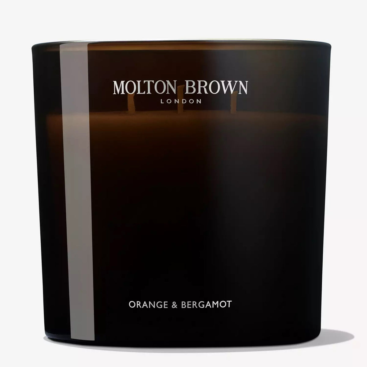 A Molton Brown - Orange and Bergamot Luxury Candle in a dark glass container. The label on the candle reads &quot;Molton Brown London&quot; at the top and &quot;Orange &amp; Bergamot&quot; at the bottom. Three wicks emit a citrus fragrance with notes of orange neroli.