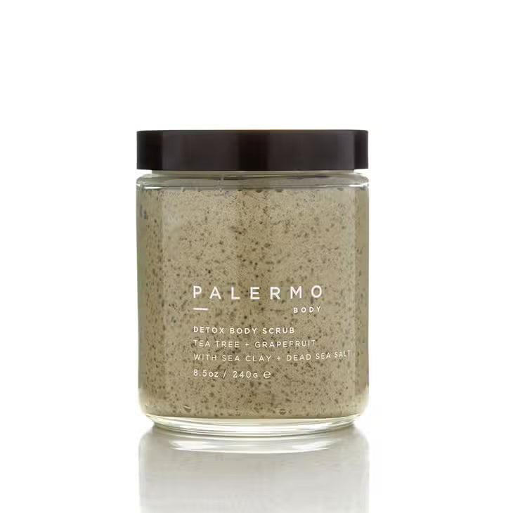 A glass jar of Palermo Body's Tea Tree and Grapefruit Body Scrub with a black lid contains 8.5 oz (240 g) of a grainy, moisturizing mixture. The label reads "Palermo Body Detox Body Scrub Tea Tree + Grapefruit with Sea Clay + Dead Sea Salt.