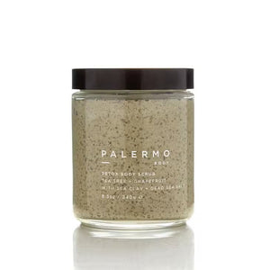 A glass jar of Palermo Body's Tea Tree and Grapefruit Body Scrub with a black lid contains 8.5 oz (240 g) of a grainy, moisturizing mixture. The label reads "Palermo Body Detox Body Scrub Tea Tree + Grapefruit with Sea Clay + Dead Sea Salt.
