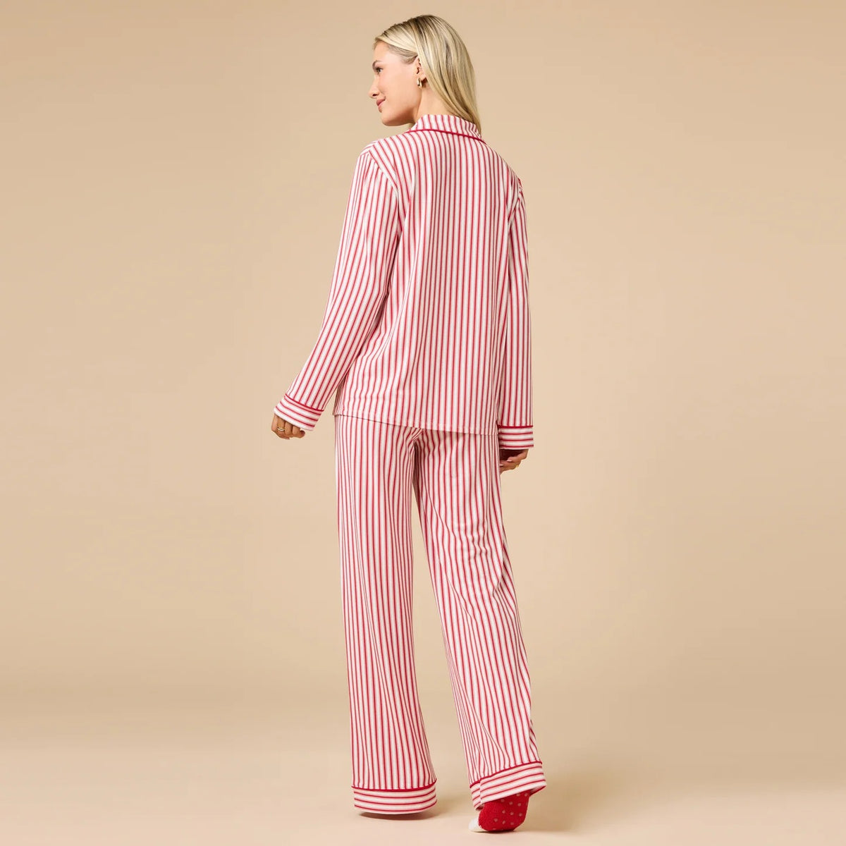 A woman wears the SOFTIES ARIA SLIM NOTCH COLLAR PJ SET, featuring a long-sleeved button-down top and matching wide-leg pants in red and white vertical stripes with red piping details.