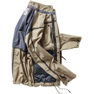 A person wearing the RELWEN Sailcloth Tanker in Desert Khaki stands on a wooden walkway, hands in pockets, with trees and sunlight in the background.