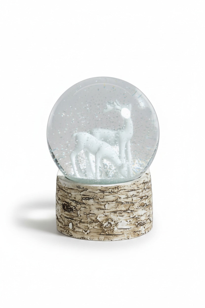 ZODAX SNOW GLOBE ON BIRCH WITH WHITE REINDEERS featuring two reindeer figures inside a glass globe set on a cylindrical, bark-textured birch base.
