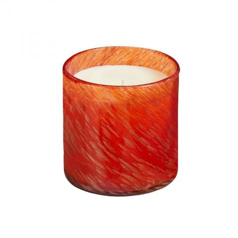 A glowing, orange-colored candle made from soy wax is placed next to a red box labeled &quot;LAFCO - ABSINTHE PLUM HOLIDAY CANDLE 15.5OZ.&quot; The scent of black plum and sandalwood permeates the air. The candle&#39;s warm, inviting glow is beautifully enhanced by the rich red background.