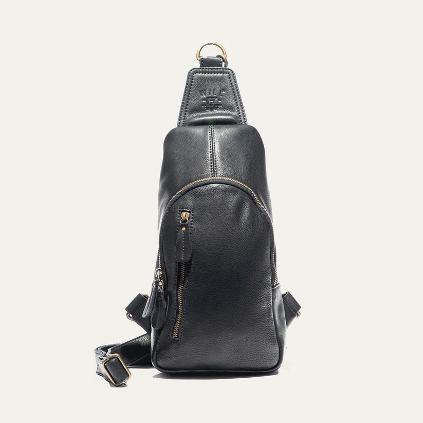 The WILL LEATHER GOODS - ZIP AROUND SLING BAG IN BLACK is a full-grain leather sling bag with gold zippers and buckle, small front pocket, adjustable strap, and top hanging loop, shown against a plain white background.