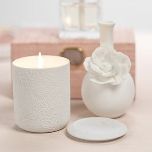 The CAMEO LONG NECK PORCELAIN BUD VASE by ZODAX is a round, white vase with a matte finish, featuring a narrow neck and a detailed floral embellishment on the front.