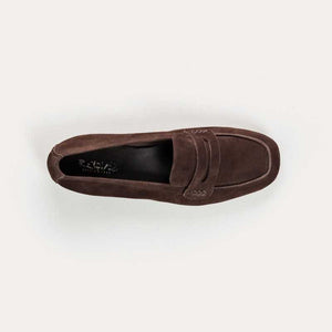 A person stands on a light floor wearing rolled-up blue jeans and REQINS HEMA suede loafers in Marron, showcasing the artisanal craftsmanship of REQINS.
