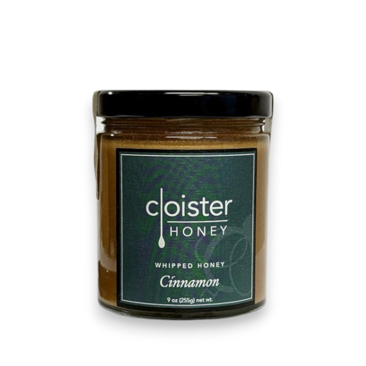 A jar of CLOISTER HONEY - WHIPPED CINNAMON HONEY 9OZ. The jar has a black lid and a green label with white lettering. Perfect as a breakfast spread, the jar contains 9 ounces (255 grams) of product.