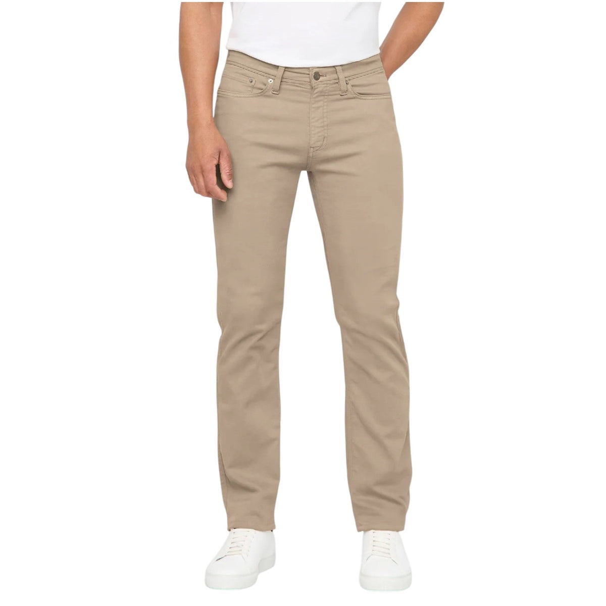 A person wearing DUER NO SWEAT STRAIGHT PANTS IN DESERT KHAKI, a white t-shirt, and white sneakers stands against a plain light gray background.