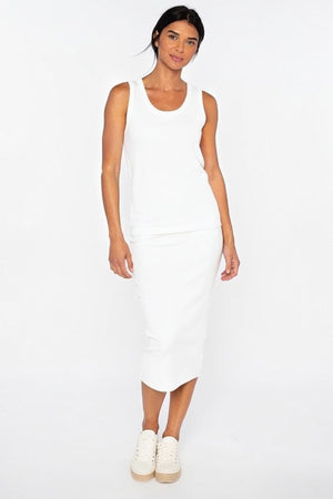 A woman stands against a plain white background, wearing the KINROSS CASHMERE Linen Rib Tank—a sleeveless white top—paired with a white midi skirt crafted from 100% linen and white sneakers. Her dark hair is pulled back and she is smiling slightly. FINAL SALE.