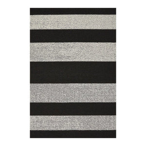 The CHILEWICH Black and White Bold Stripe Shag Doormat (18x28) rests on a light floor, with a pair of black flip-flops positioned to the right of the mat. Horizontal white wall panels provide a background.