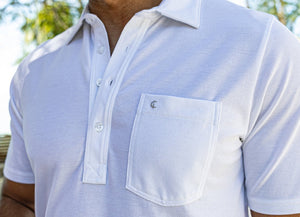A man with dark hair and a short beard wears the CRIQUET Oxford Pique Players Shirt in white and green shorts, standing against a plain white background and smiling.
