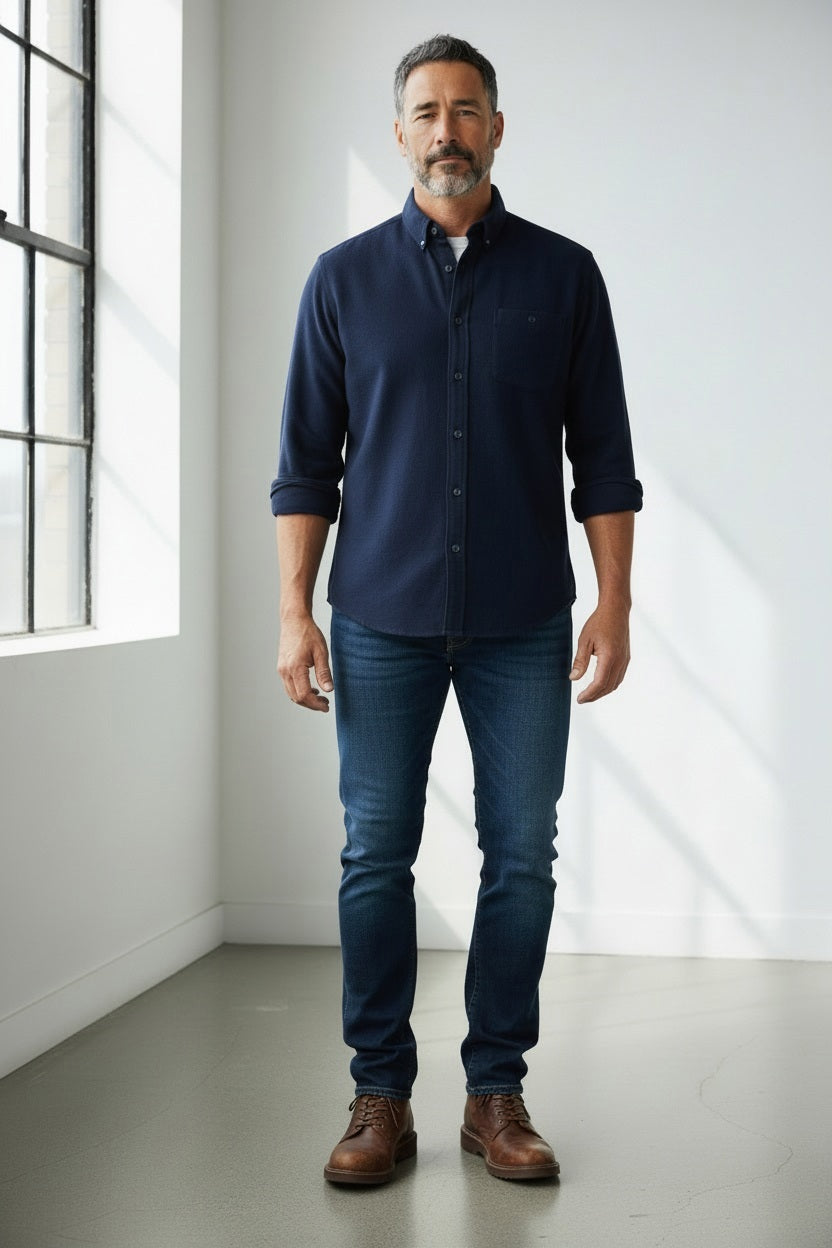 A man wearing a FRANK AND EILEEN - DON MEN’S BUTTON UP SHIRT IN ITALIAN FLANNEL NAVY, dark blue jeans, and brown leather boots.