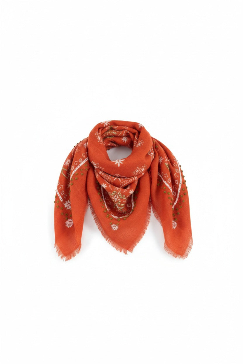 The STORIATIPIC - NELLY WOOL BANDANA SCARF by STORIATIPIC is an orange wool accessory measuring 100x100 cm, featuring fringed edges and adorned with white and pink floral embroidery accented with green details. Elegantly arranged in a loose loop on a white background, this scarf offers both style and comfort.