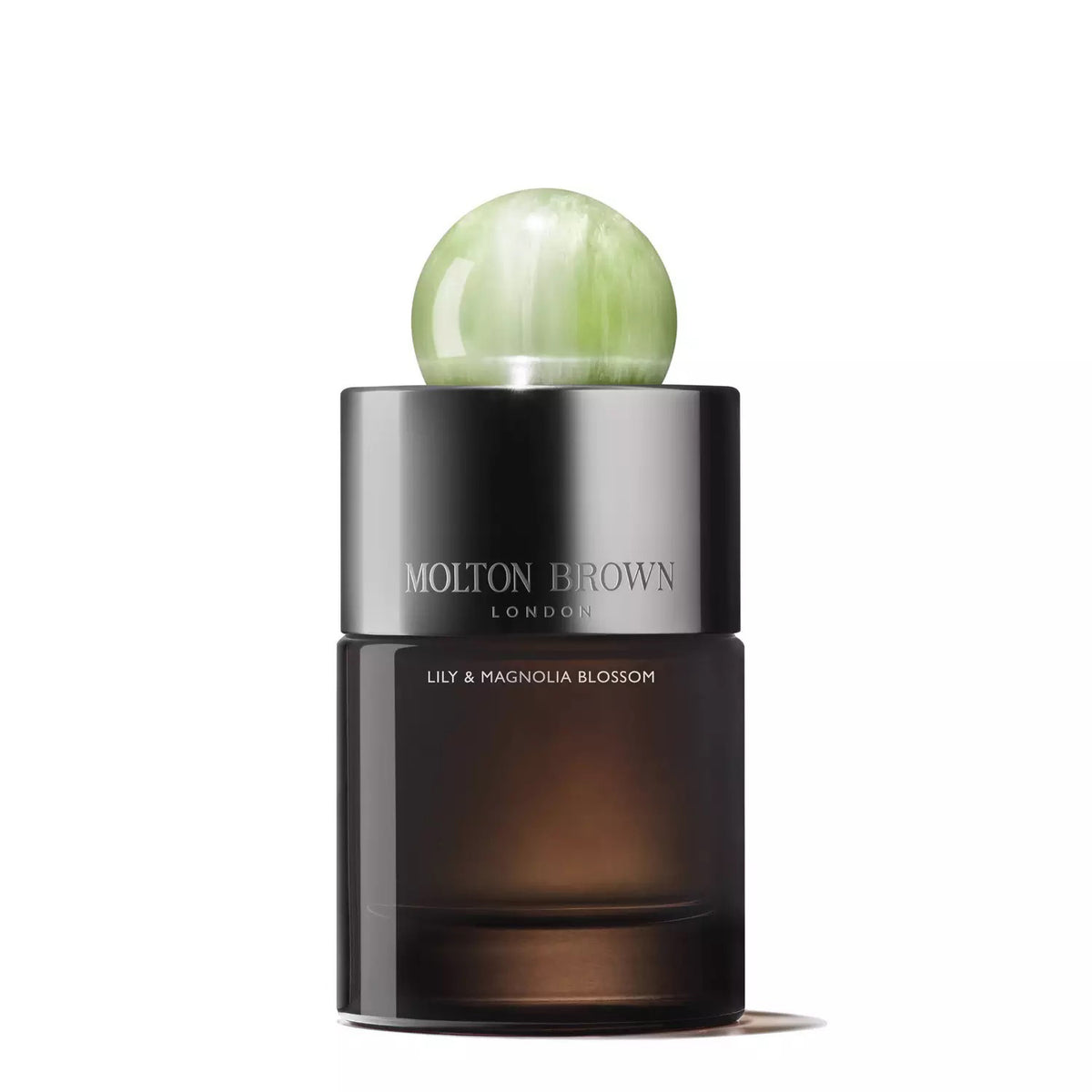The MOLTON BROWN - LILY AND MAGNOLIA BLOSSOM EAU DE PARFUM boasts a dark, translucent bottle featuring a metallic cap and topped with a decorative green sphere, exuding an elegant, modern aesthetic. This floral fragrance from MOLTON BROWN perfectly captures sophistication.