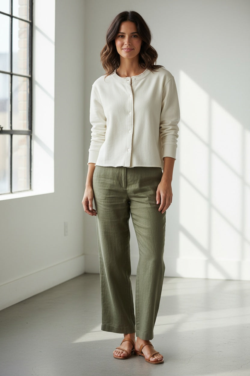 A woman with light brown hair stands with her back to the camera, wearing the FRANK &amp; EILEEN Jackie Sweatshirt Cardigan in Triple Fleece Vintage White and a navy blue skirt, in front of a stone building with arched columns and a window.
