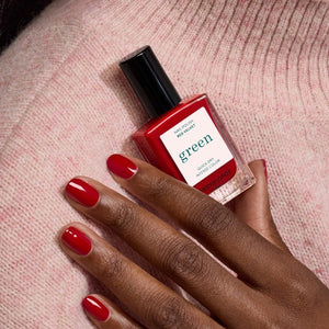 A hand with neatly manicured nails painted in MANUCURIST - GREEN™ NAIL POLISH IN RED VELVET by MANUCURIST INC rests on a textured red leather surface, creating a coordinated and stylish look.