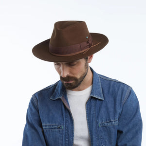 The WYETH - TEDDY HAT IN BROWN by WYETH is a vintage-inspired wide-brimmed fedora with a matching dark brown ribbon band, shown against a plain white background.