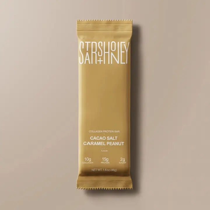A gold wrapper labeled “STARS+HONEY” collagen protein bar in Cacao Salt Caramel Peanut flavor is centered on a beige background, highlighting its indulgent peanut chocolate appeal with added health benefits. Boasting 10g collagen, 15g protein, and just 2g sugar per 1.8 oz (52g) bar, this low sugar STARS+HONEY-CACAO SALT CARAMEL PEANUT protein snack combines delicious taste with functional nutrition.