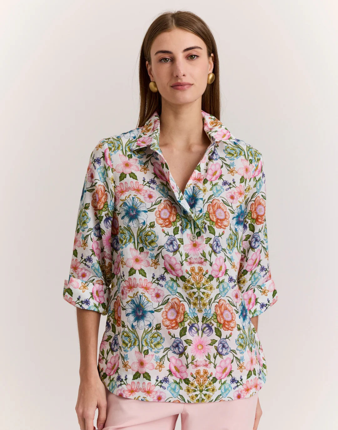 A woman with straight brown hair wears the HINSON WU - CHARLOTTE 3/4 SLEEVE LINEN SHIRT IN BOTANIQUE PRINT, paired with light pink pants, standing against a plain light background.