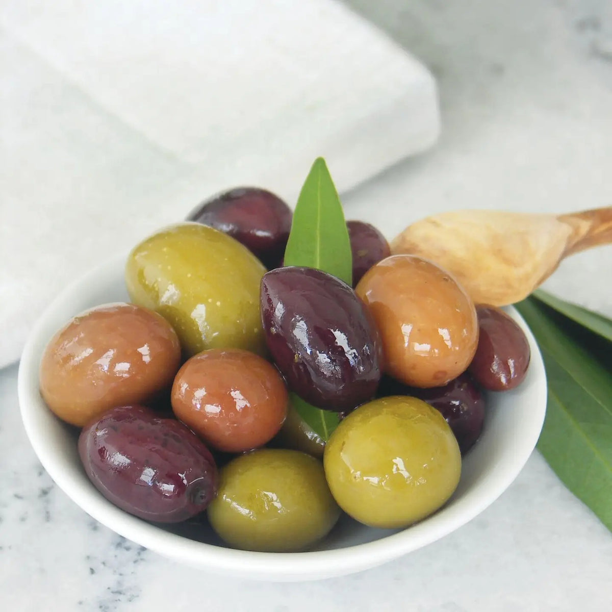 A glass jar of DIVINA - GREEK OLIVE MIX, featuring a green label and filled with assorted, traditionally cured Greek olives, set against a white background.