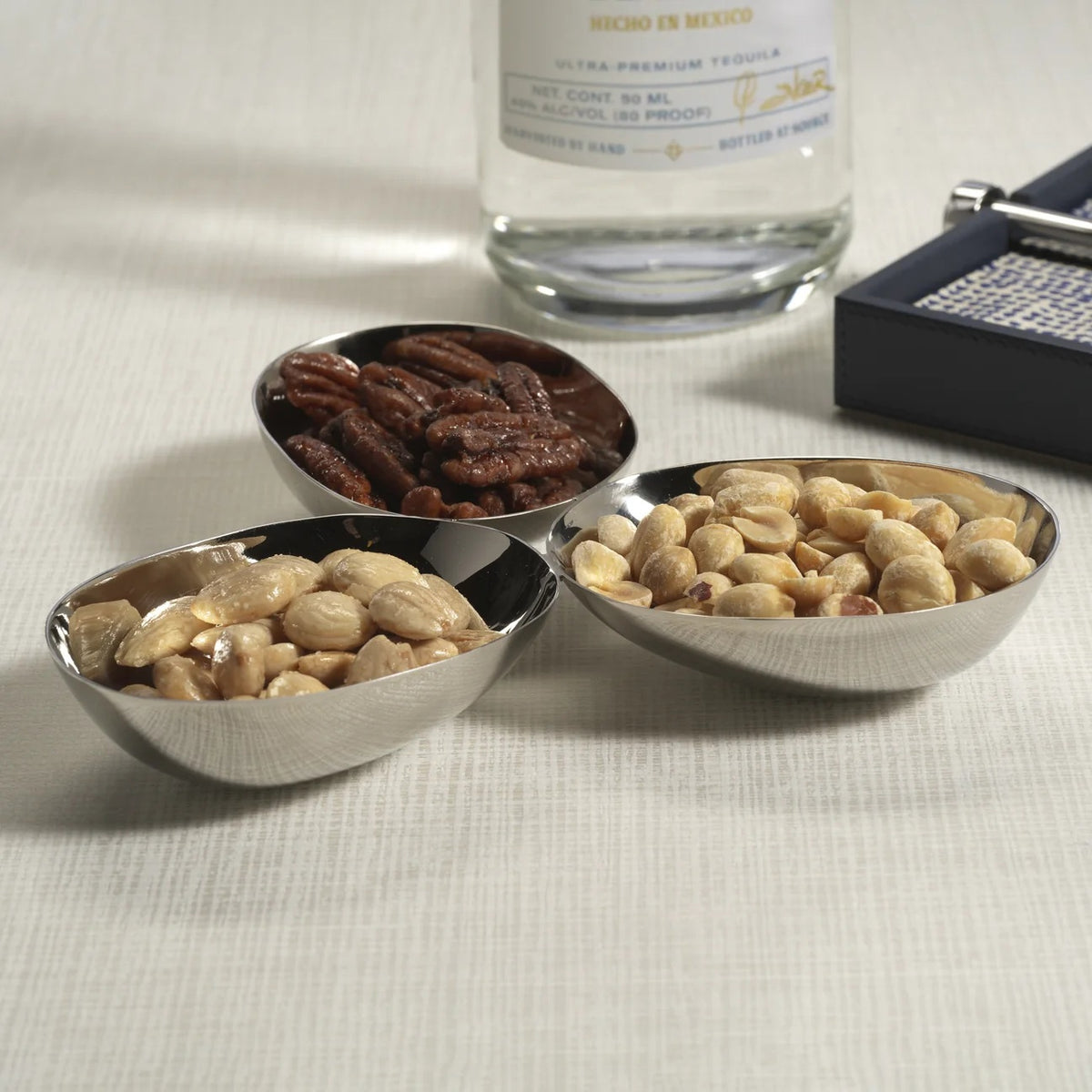 Three connected, polished nickel TRIPLE NUT BOWL alloy bowls arranged in a cluster on a square plate.
