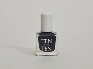 A glass bottle of TENOVERTEN - NAIL POLISH from the brand TEN OVER TEN, featuring a white cap and a dusty pink nail color. The front label displays "TEN OVER TEN" in white uppercase letters. This vegan, eight-free formula ensures both beauty and peace of mind. The background is plain and light-colored.