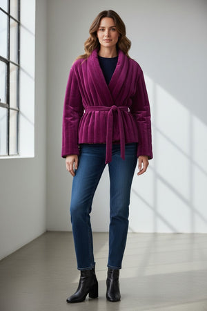 A woman stands indoors near large windows, smiling while wearing the FRANCO FERRARI REVERSIBLE KIMONO JACKET with a botanical floral print, styled with a purple belt, white top, blue jeans, and brown ankle boots.