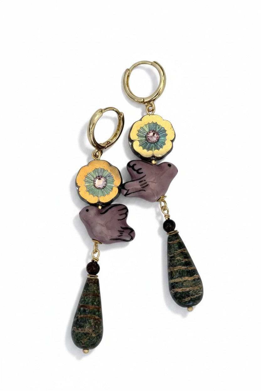 SANDRINE FRANCE STUDIO - AURORA EARRINGS: Mismatched gold hoop earrings by SANDRINE FRANCE STUDIO, each featuring a playful mix of charms including a flower, a purple bird, and a green teardrop stone for a whimsical, colorful look.